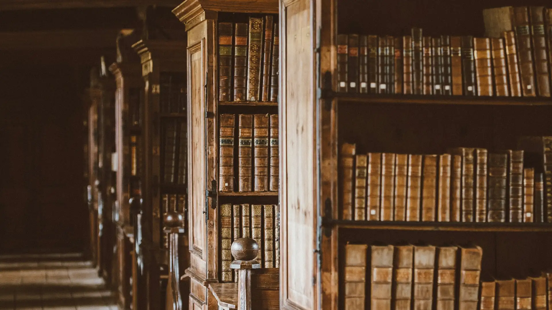 A dim library aisle with old bound books on wooden shelves